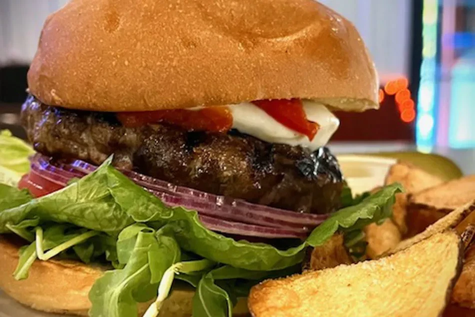 Char-grilled burger with arugula, peppers, cheese, wedges, and pickle.
