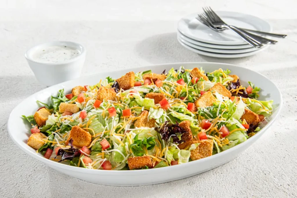 Large salad with lettuce, cheese, tomatoes, and croutons in a white bowl.