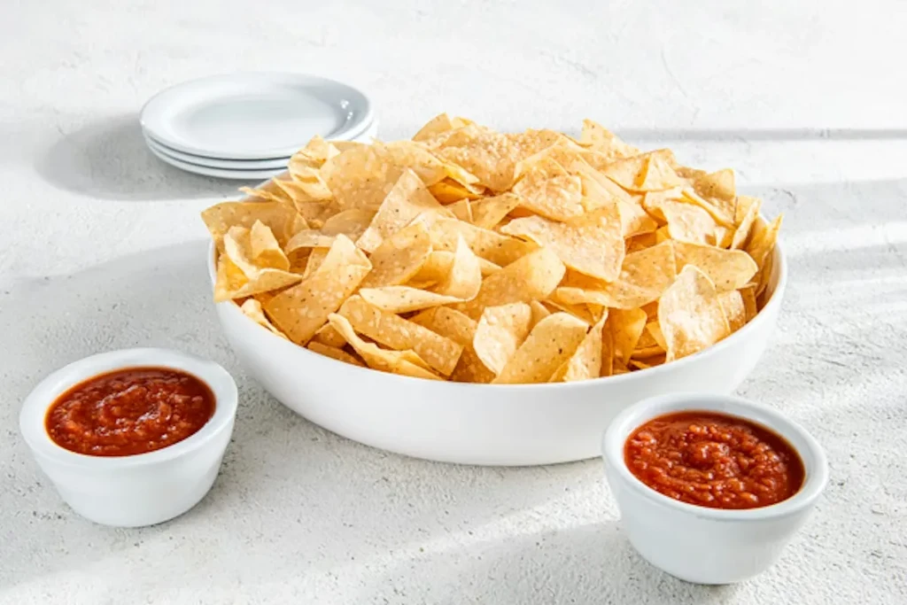 Bowl of tortilla chips with two ramekins of salsa.