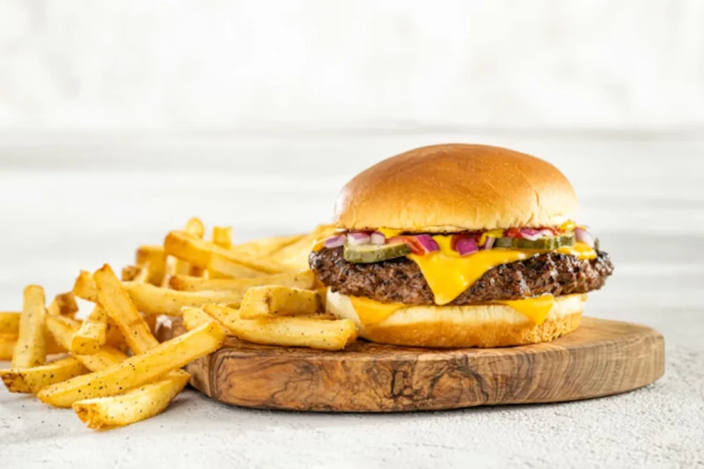 Cheeseburger with melted cheese, onions, and pickles, next to french fries.