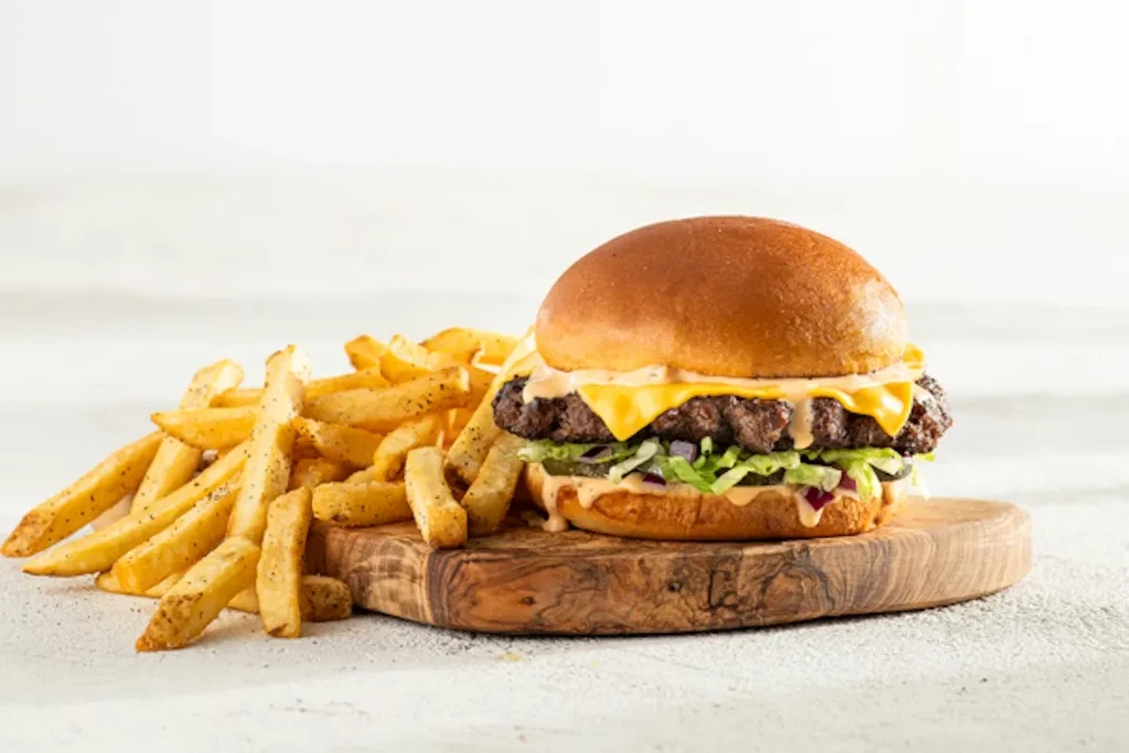 Cheeseburger and french fries on a wooden cutting board.