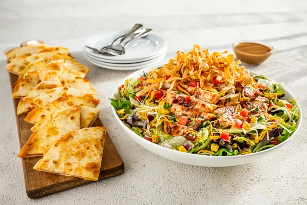 Salad with grilled chicken and quesadilla slices on a wooden board.