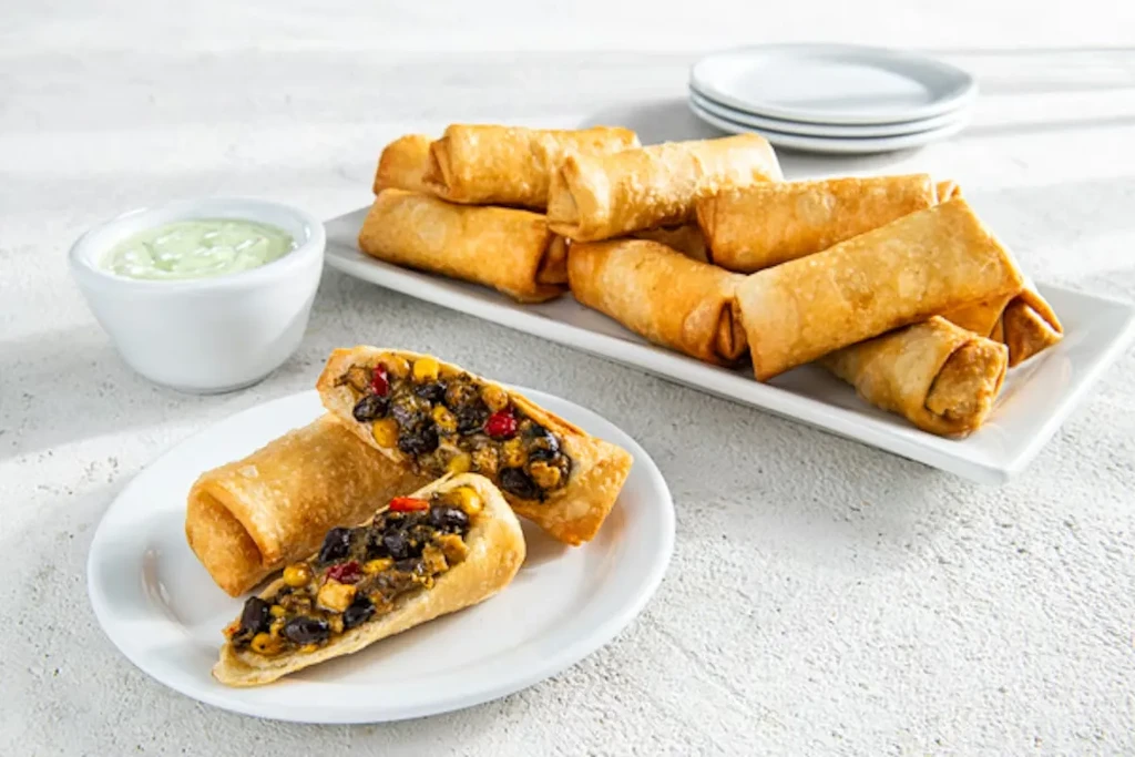 Egg rolls with black beans, corn, and a green dipping sauce.