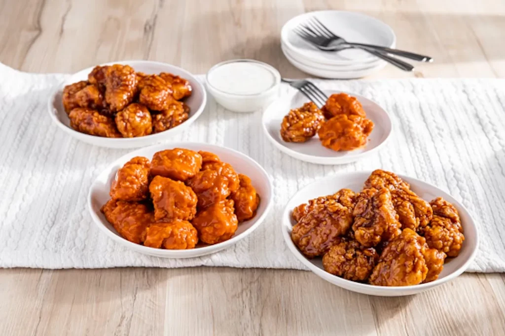 Multiple bowls of chicken wings with orange and brown sauces.