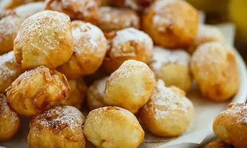 Pile of golden brown fried pastries heavily dusted with powdered sugar.