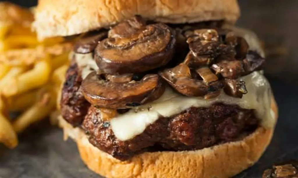 Close-up burger with thick patty, melted cheese, mushrooms, and fries.