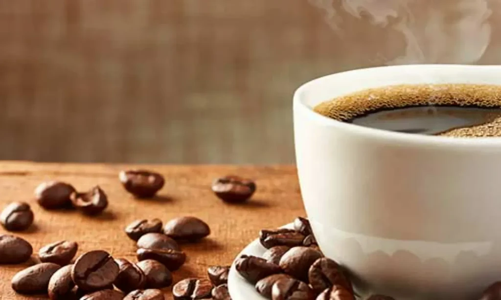 Steaming white coffee cup with foam and roasted beans on wood.