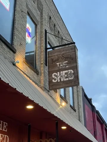 Hanging wooden sign "Food & Spirits THE SHED" on a brick building.