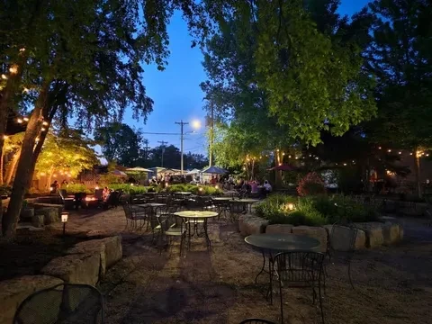 Rustic outdoor dining area at dusk, lit by warm string lights.