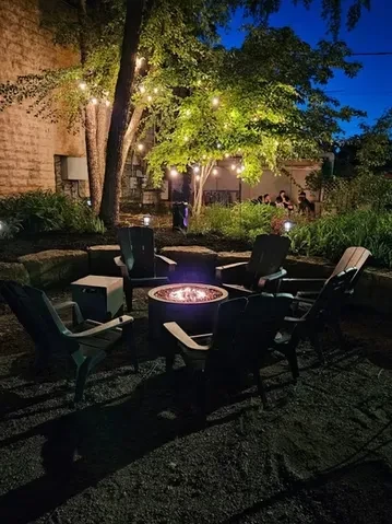 Outdoor fire pit with Adirondack chairs under string lights at night.