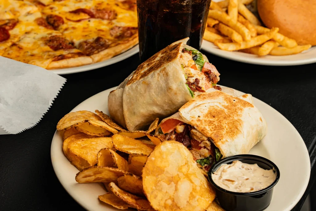 Chicken wraps, chips, dip, pizza, fries, and beverages on a table.