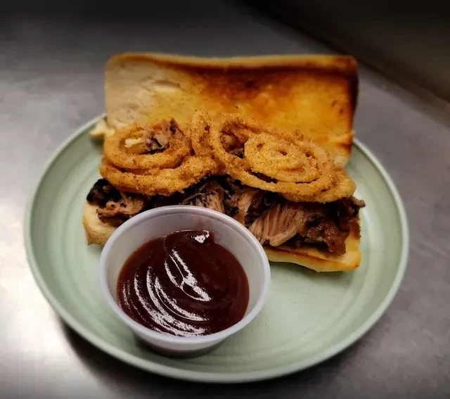 Toasted shredded meat sandwich with onion rings and barbecue sauce.