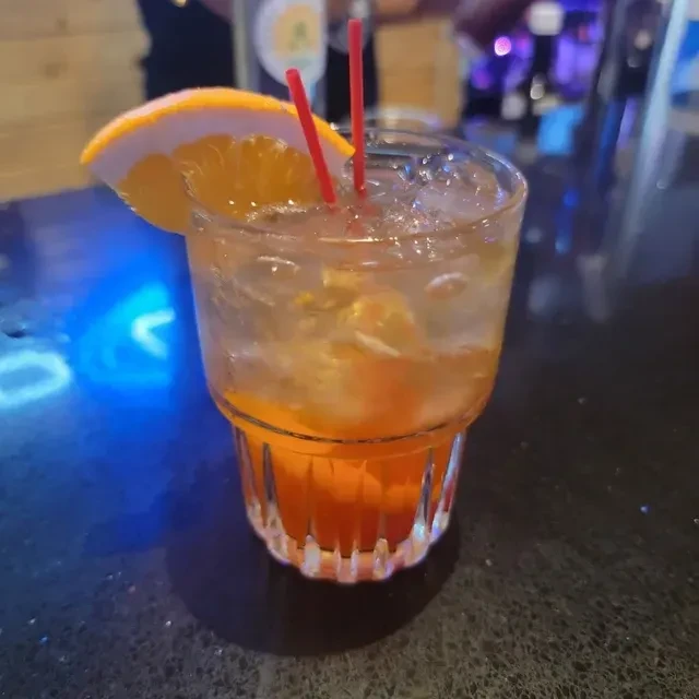 Orange cocktail in a faceted glass with ice and orange slice.