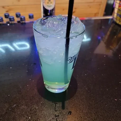Miller Lite glass with blue-green drink, crushed ice, on a dim bar.