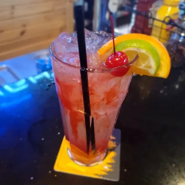 Vibrant pink cocktail with cherry and citrus garnishes on a dark counter.