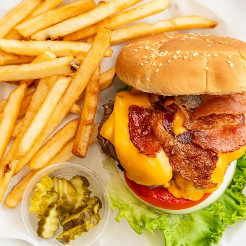 Top-down view of a loaded bacon cheeseburger, french fries, and dill pickles.