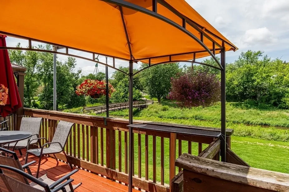 Orange-canopied deck with dining tables overlooks a green landscape and river.