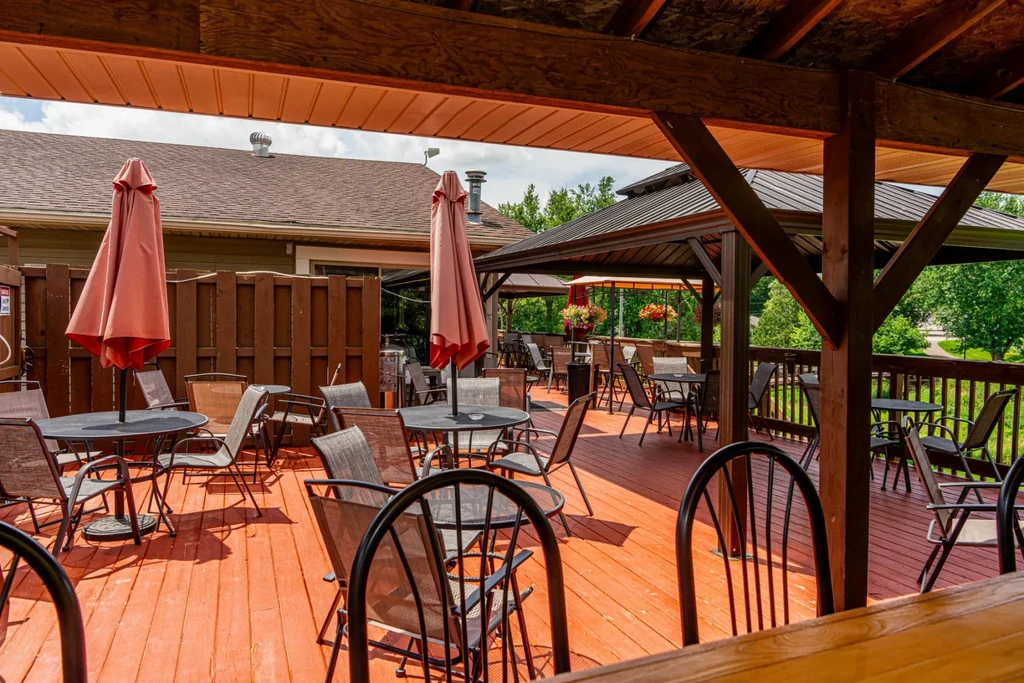 Empty sunny patio with wooden deck, tables, and pink umbrellas.