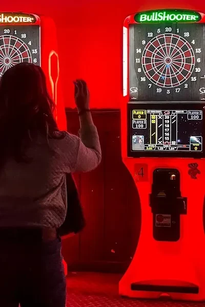 Rear view of person throwing dart at red-lit arcade machine.