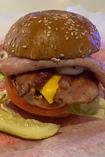 Large burger with melted cheese, bacon, tomato, lettuce, and a pickle.