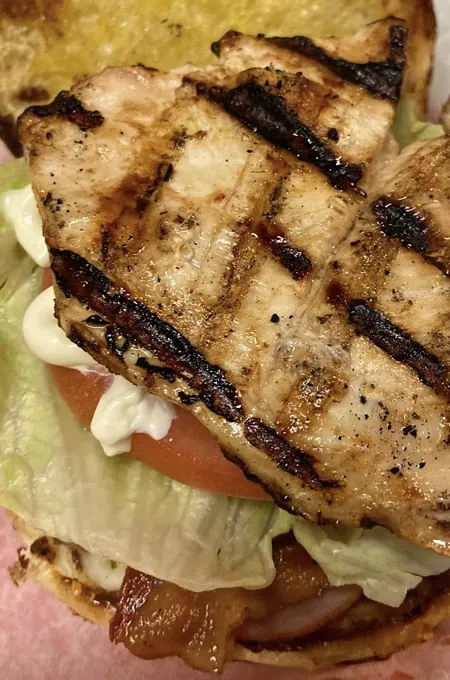 Close-up grilled chicken sandwich with bacon, lettuce, tomato, and sauce.