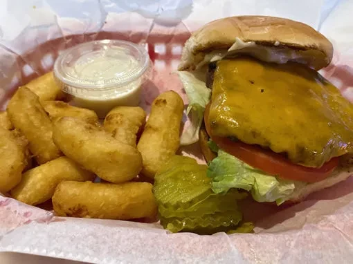 A cheeseburger, fries, sauce, and pickle in a red basket.