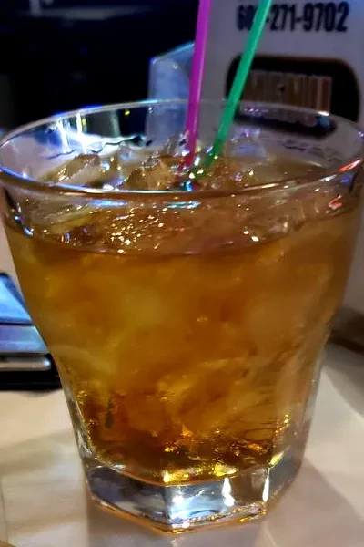 Dark amber drink in faceted glass with ice and pink/green straws.