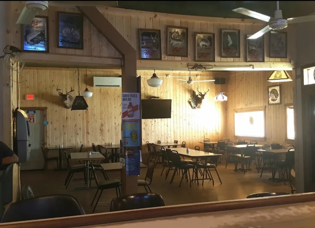 Rustic bar interior with empty tables, deer heads, and person at bar.