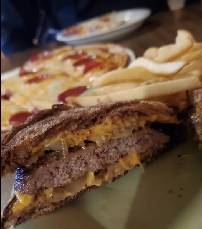 Patty melt sandwich, cut in half, with fries on a green plate.