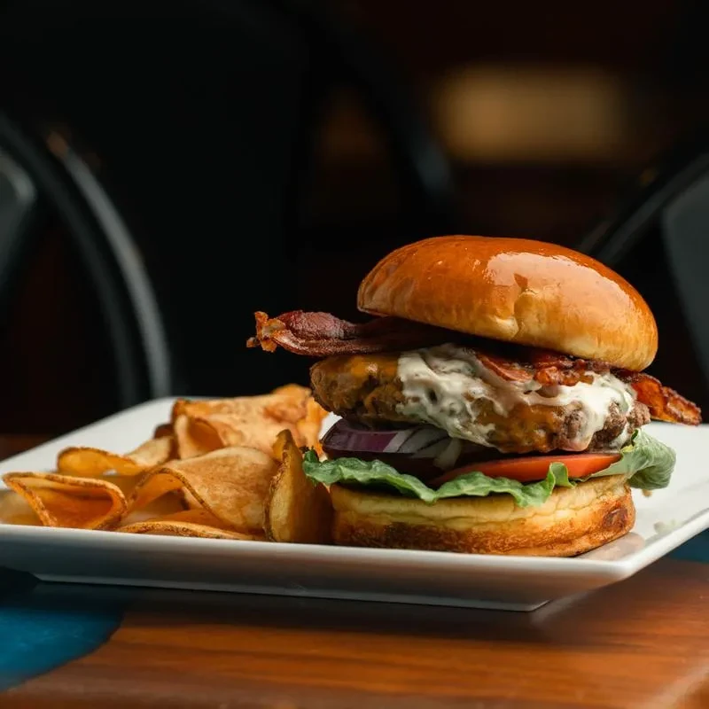 Close-up: Brioche burger, bacon, melted cheese, potato chips.
