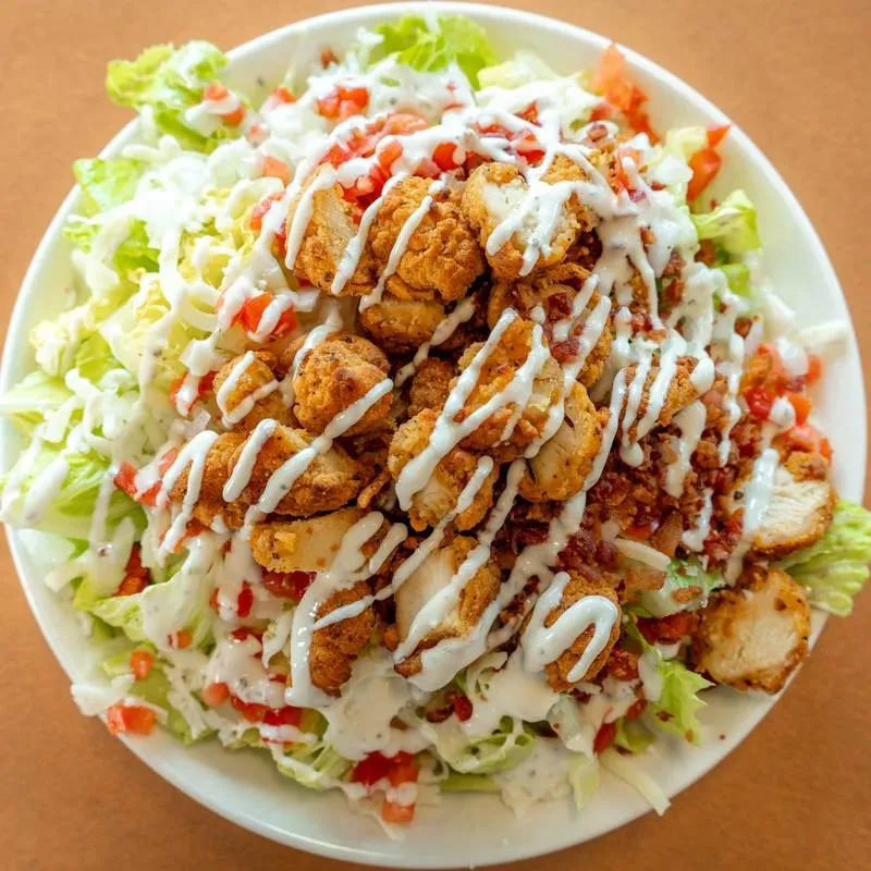 Overhead fried chicken salad with lettuce, tomatoes, creamy dressing, and bacon.