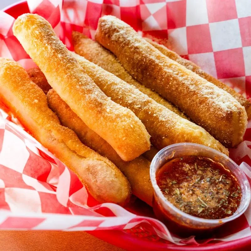 Golden-brown Parmesan breadsticks with marinara sauce in a red basket.