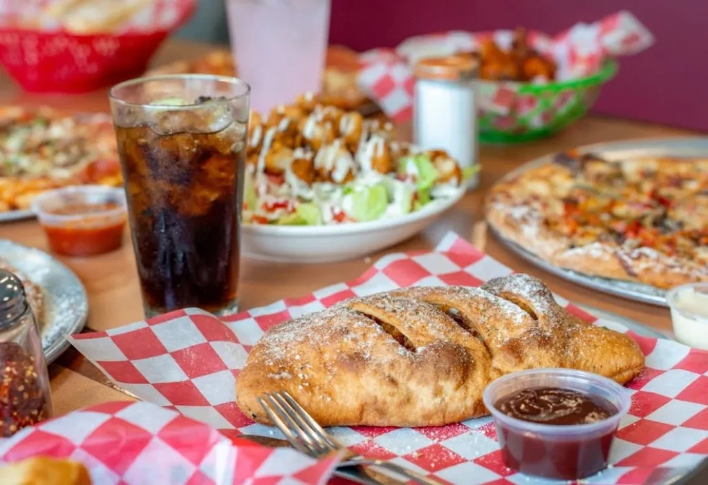 Large calzone, salad, soda, pizza, and wings on a wooden table.