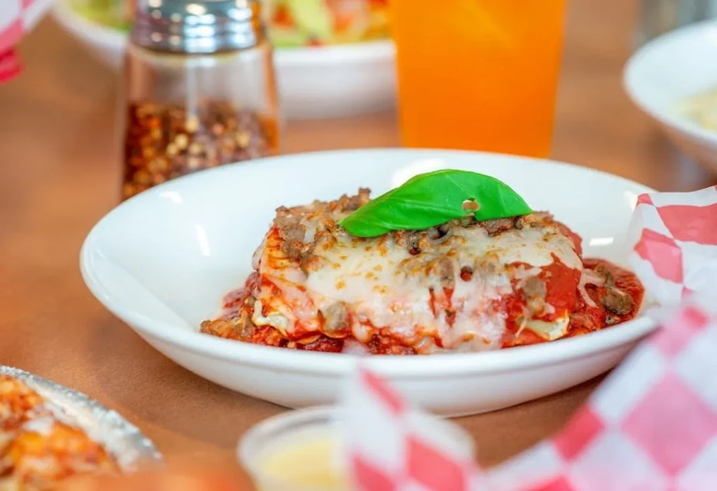 Close-up of lasagna in a white bowl with basil, cheese, and meat.