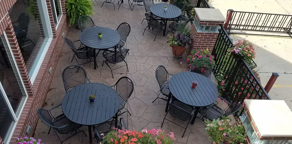 Overhead view of outdoor patio with dark tables, chairs, and colorful flowers.