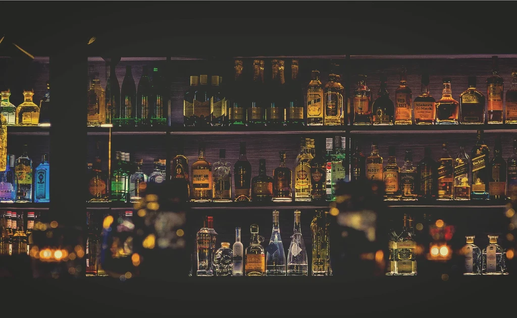 Dark bar shelves filled with numerous glowing bottles of diverse spirits.