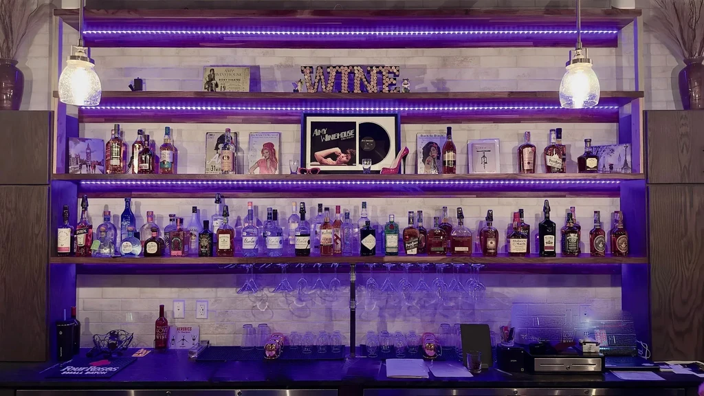 Multi-tiered bar shelves with liquor, glasses, and purple LED lighting.