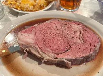 Medium-rare prime rib on a plate with au jus and a knife.