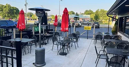 Empty outdoor restaurant patio with black dining furniture, red umbrellas, heater.