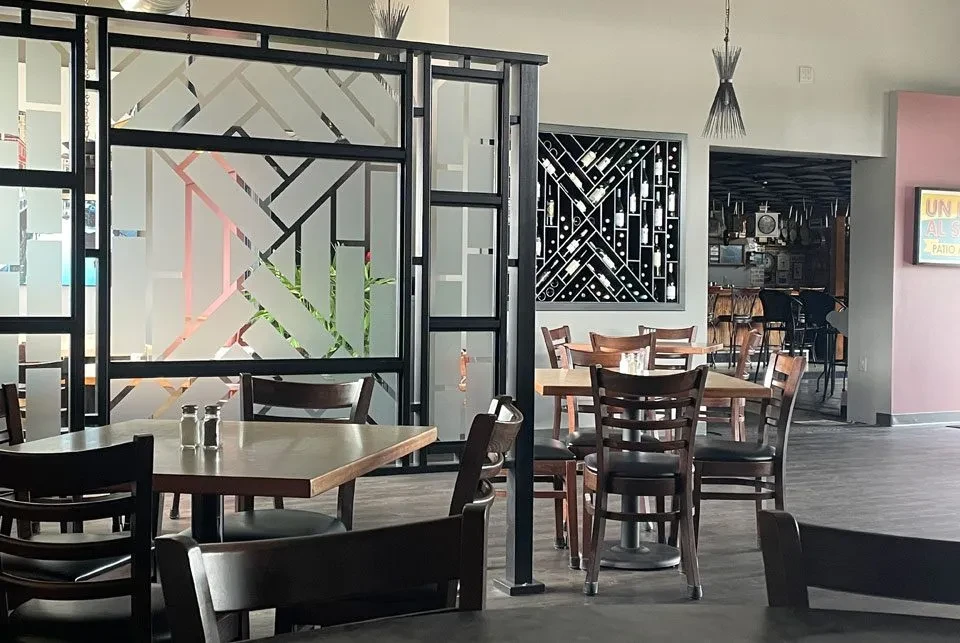 Empty modern restaurant interior with dining tables, a wine rack, and frosted partition.