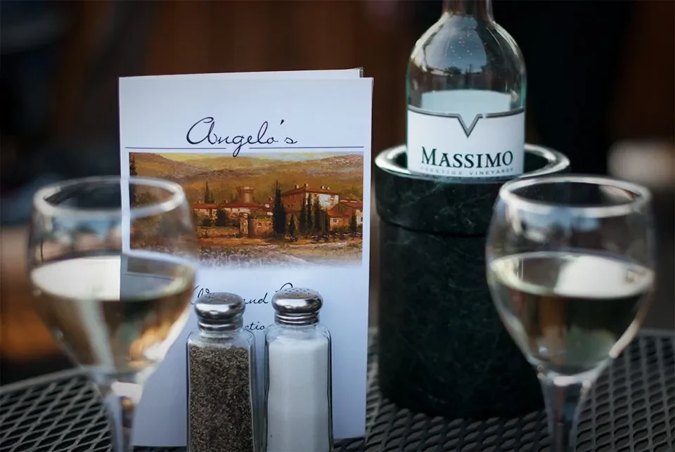 White wine bottle in chiller, two glasses, and Angelo's menu.