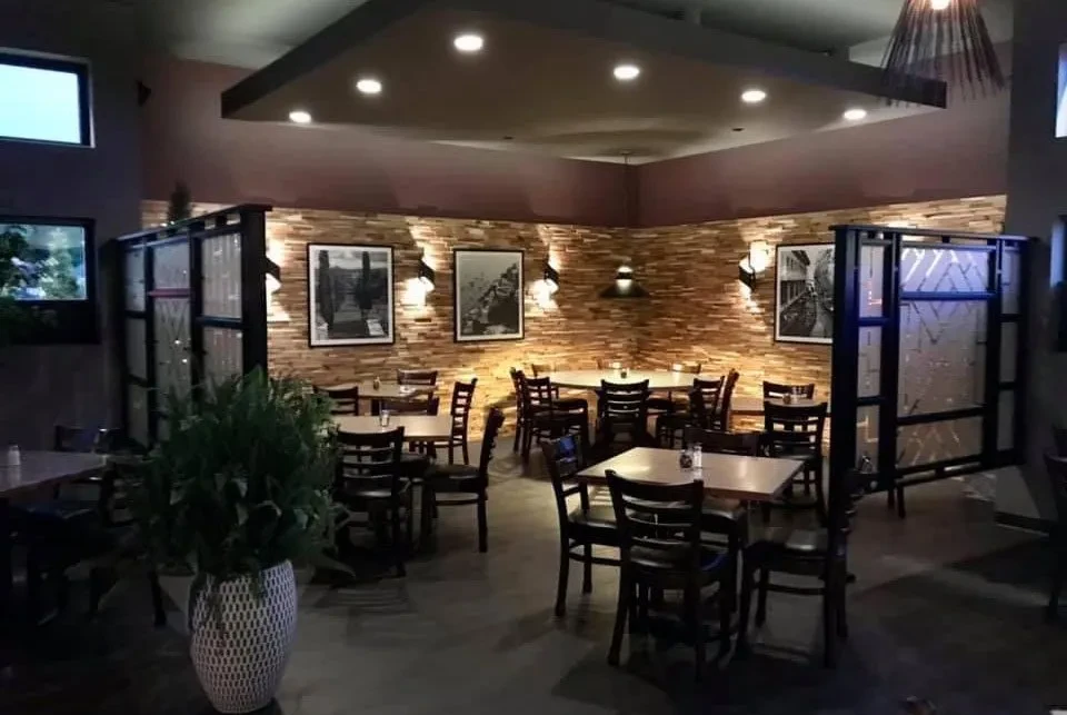 Warmly lit modern restaurant interior with wooden accent wall and dining tables.