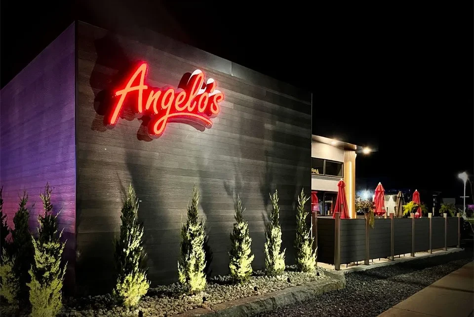 Modern Angelo's restaurant exterior at night with red neon sign and patio.