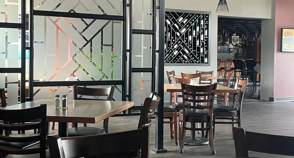 Bright, modern restaurant interior with dining tables, wine rack, and bar.