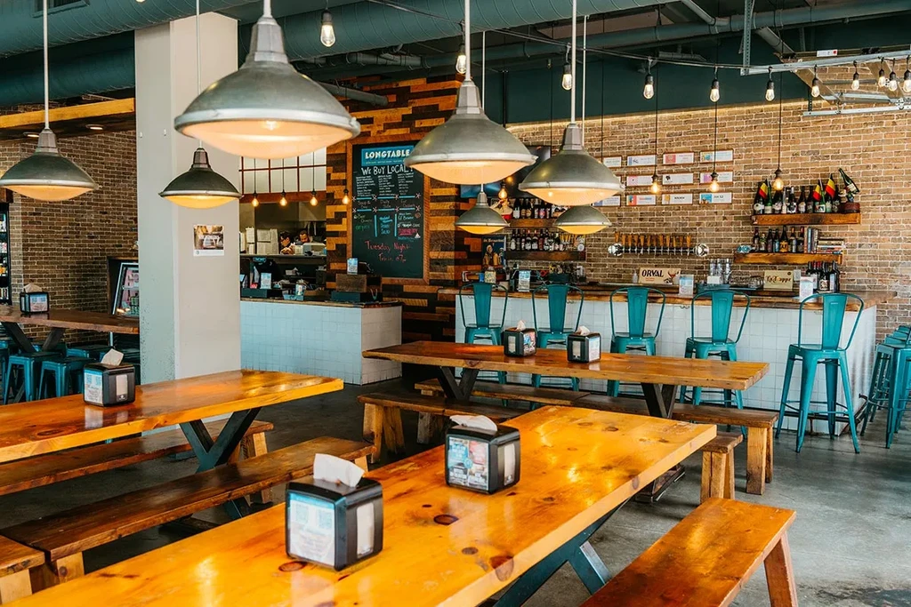Industrial-style brewpub interior with long wooden tables, a bar, and exposed brick.