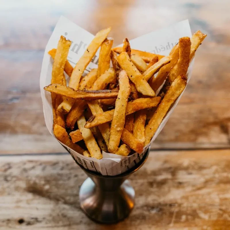 French fries in a patterned paper cone and metal goblet.
