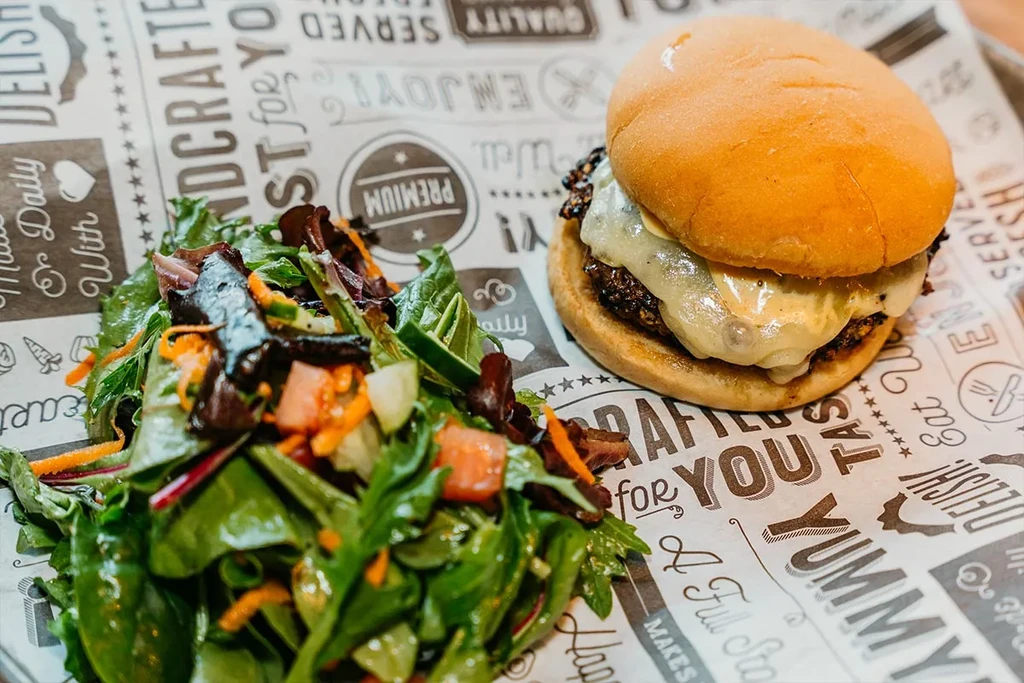 Cheeseburger and side salad on branded parchment paper.