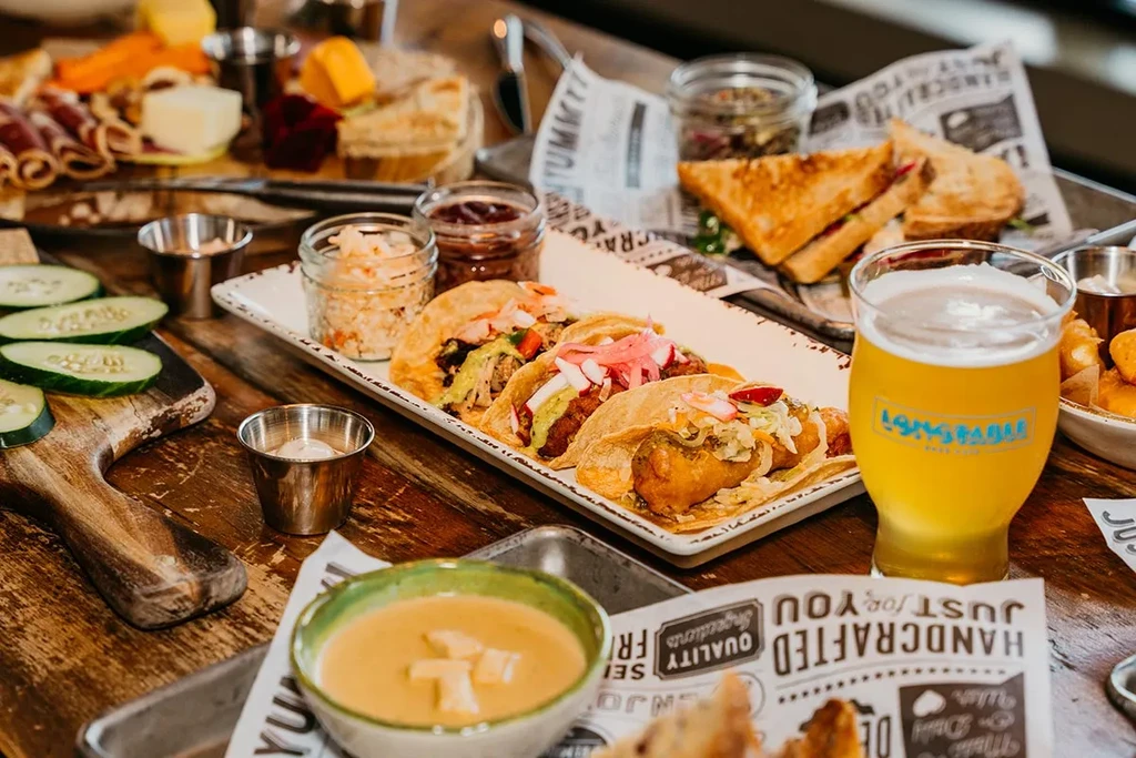 Rustic table with beer, tacos, charcuterie, grilled cheese, and soup.