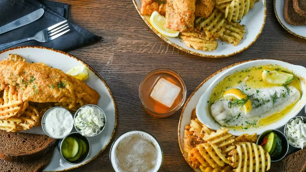 Top-down view: Rustic table with seafood dishes, fries, coleslaw, and drinks.