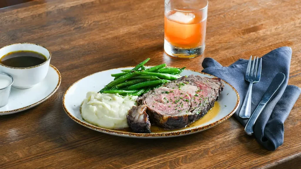 Rare prime rib, mashed potatoes, and green beans on a wooden table.